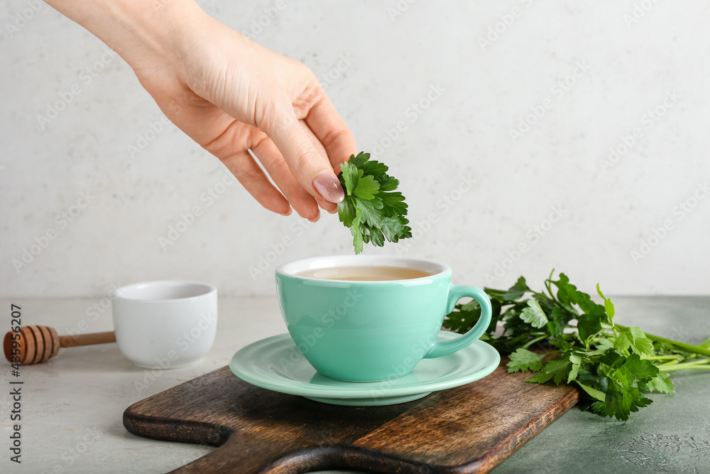 Woman preparing hot tea with parsley on light background Woman preparing hot tea with parsley on light background