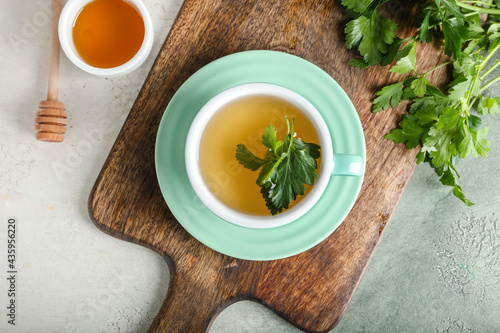 Board with cup of hot tea, parsley and honey on light background