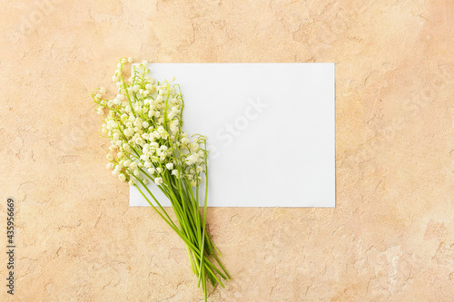 Blank card and beautiful lily-of-the-valley flowers on color background