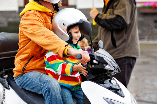 Little toddler boy with helmet and his father driving on moped in the city. Happy child as passenger on motor bicycle with dad. Safety and safe transport with children on vehicles. Man hold child.