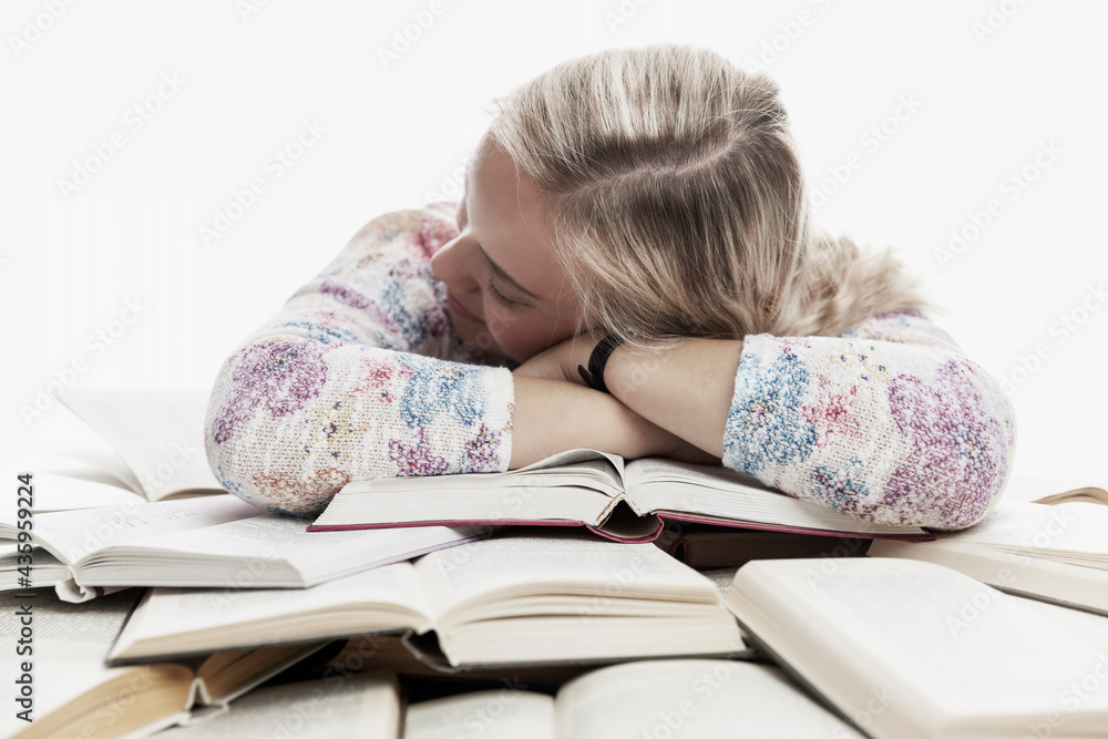 A young girl sits at a table and sleeps on books. Learning difficulties. White background. A young girl sits at a table and sleeps on books. Learning difficulties. White background.