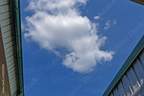 View from under the eaves of the roof to the blue sky with white clouds on a sunny spring day