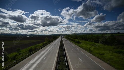 A 4K time-lapse of driving cars on a dual carriageway road through farmlands under white fluffy clouds