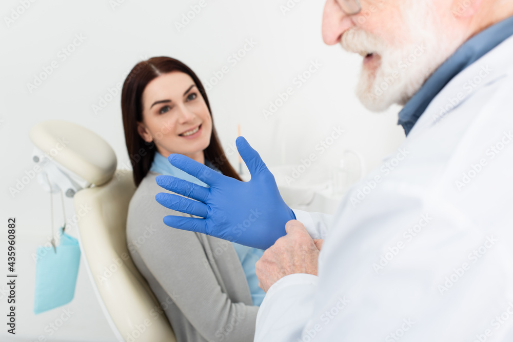 Obraz premium dentist adjusting latex gloves before examination of patient sitting in dental chair.