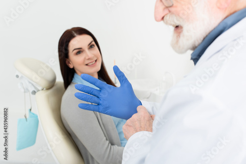 dentist adjusting latex gloves before examination of patient sitting in dental chair.
