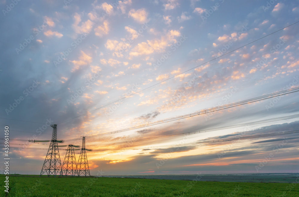 Obraz premium High voltage lines and power pylons in a flat and green agricultural landscape on a sunny day with cirrus clouds in the blue sky
