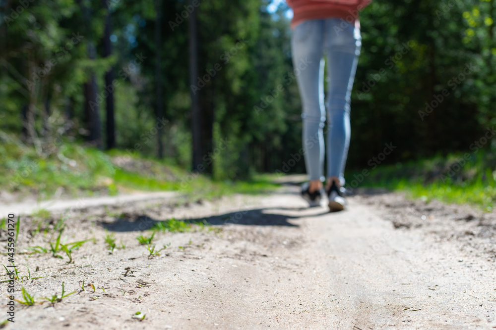 Rear view photo of female tourist legs walking in a forest road.Summer day.Selective focus. Rear view photo of female tourist legs walking in a forest road.Summer day.Selective focus.