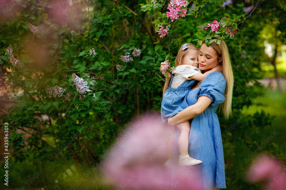 Happy mother's day. Little girl hugs her mother in the spring cherry garden. Portrait of happy mother and daughter among pink flowers trees. Family values. Motherhood. Mom and child in blooming park.
