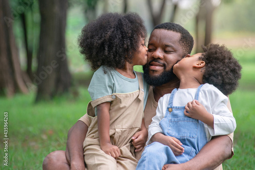 African father and daughter and son had a great time at the outdoor park, two children are sitting on the lap of the father and kiss him, Father's day © chomplearn_2001