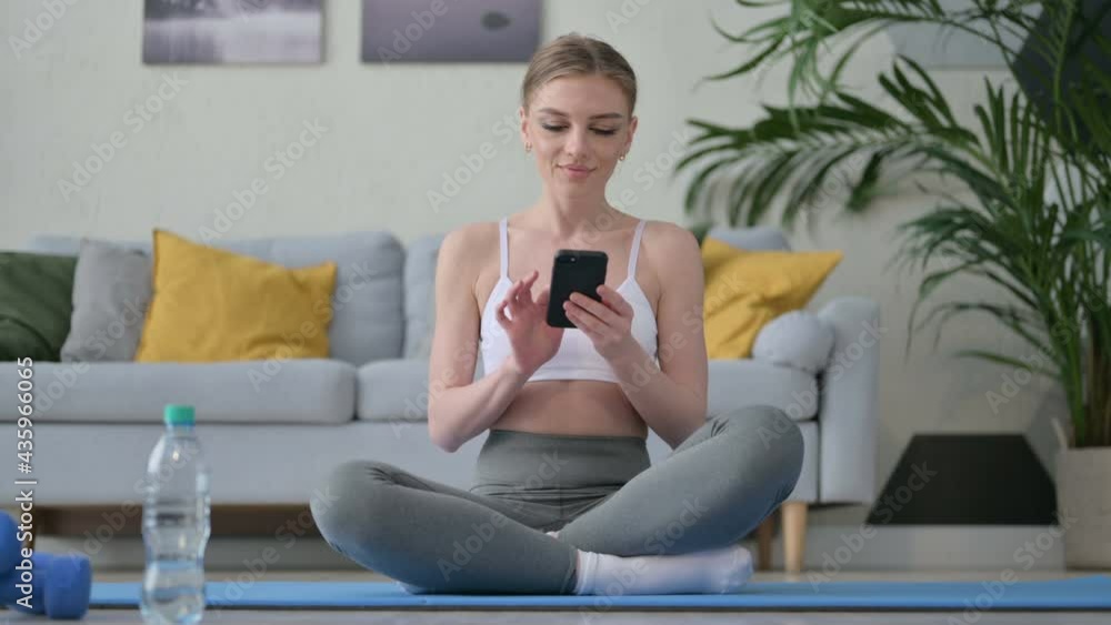 Young Woman using Smartphone on Yoga Mat at Home Young Woman using Smartphone on Yoga Mat at Home