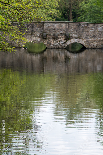 Alte Steinbrücke mit zwei Bögen über einen Wassergraben. Wunderschöne grüne Spiegelungen von den Bäumen mit frischem Frühlingslaub auf dem Wasser.