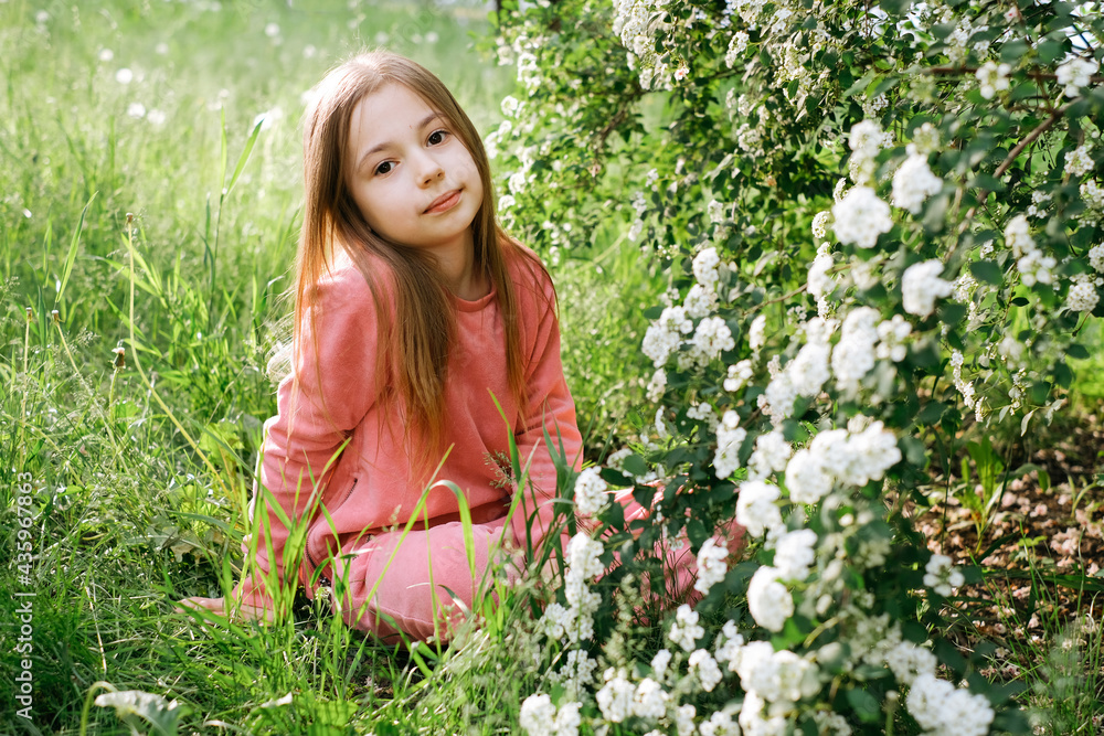 little kind girl in a pink velor suit in the spring in the park near a flowering bush with white flowers little kind girl in a pink velor suit in the spring in the park near a flowering bush with white flowers