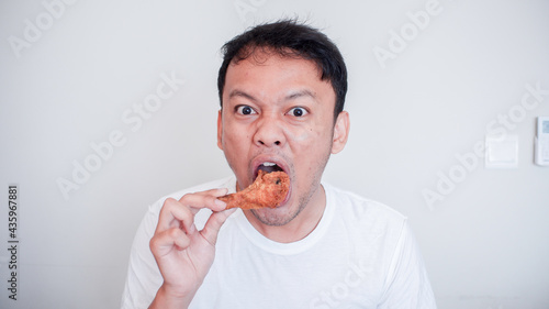 Young Asian man is eating fried chicken wear white shirt