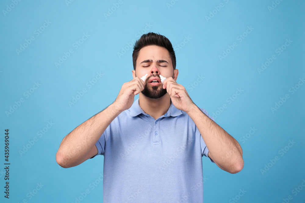 Man using nasal sprays on light blue background Man using nasal sprays on light blue background