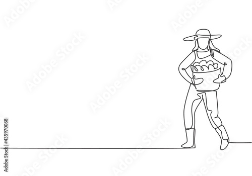 Single continuous line drawing young female farmer carrying a basket full of fruit with her hands in front of her chest. Minimalism concept. Dynamic one line draw graphic design vector illustration.