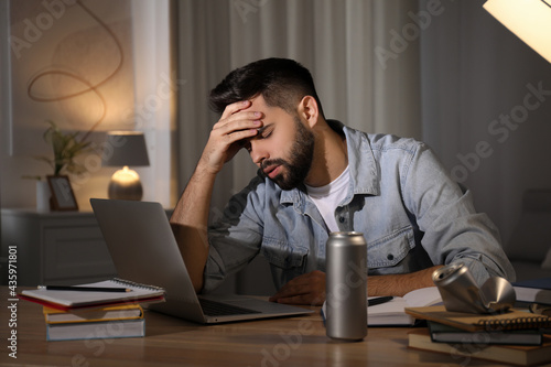 Tired young man with energy drink studying at home