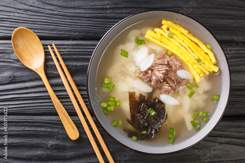 Tteokguk or sliced rice cake soup is a traditional Korean dish eaten during the celebration of the Korean New Year closeup in the bowl on the table. Horizontal top view from above photo