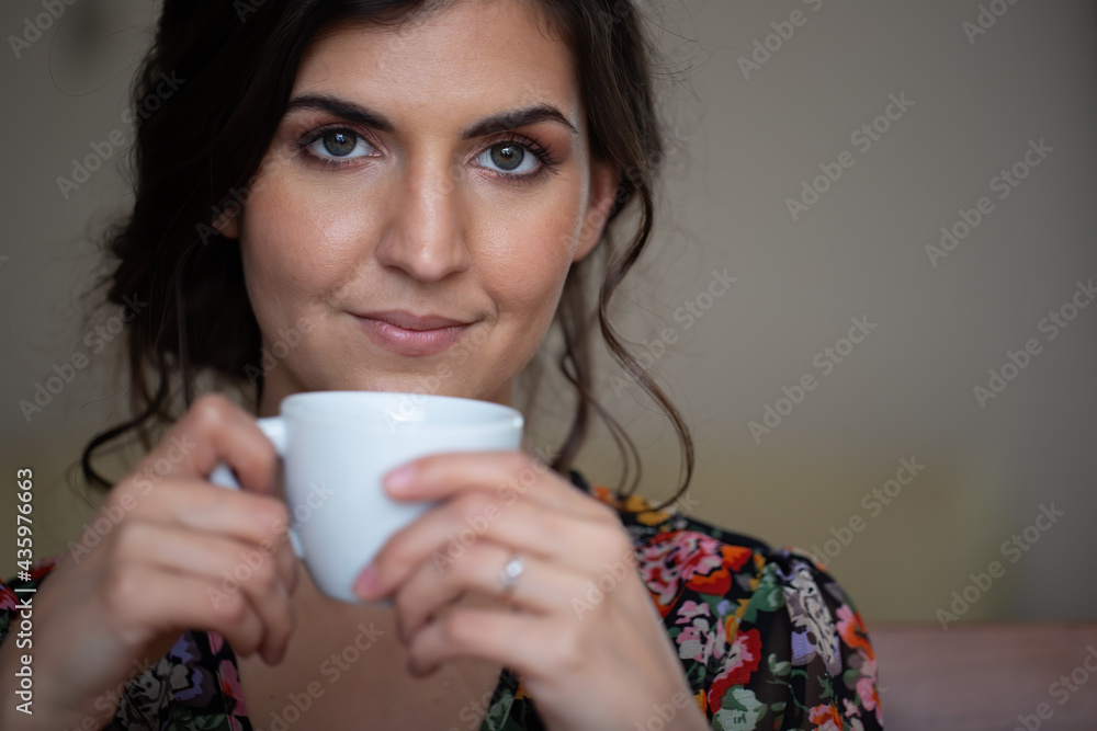 Portrait of woman holding cup with coffe in close up. Young female looking to the camera with mug at home. Head of brunette girl smiling. Portrait of woman holding cup with coffe in close up. Young female looking to the camera with mug at home. Head of brunette girl smiling.