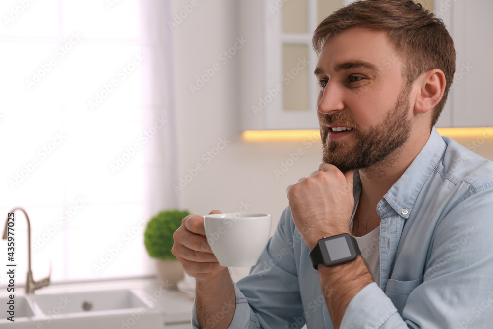 Young man with smart watch and cup of coffee in kitchen, space for text Young man with smart watch and cup of coffee in kitchen, space for text