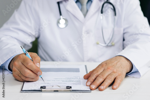 Close up wrinkled male doctor writing information in medical registration journal. Confident old mature male doctor physician therapist working at office, handwriting notes