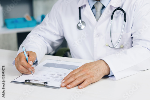Confident old mature male doctor physician therapist working at office  handwriting notes. Close up wrinkled male doctor writing information in medical registration journal