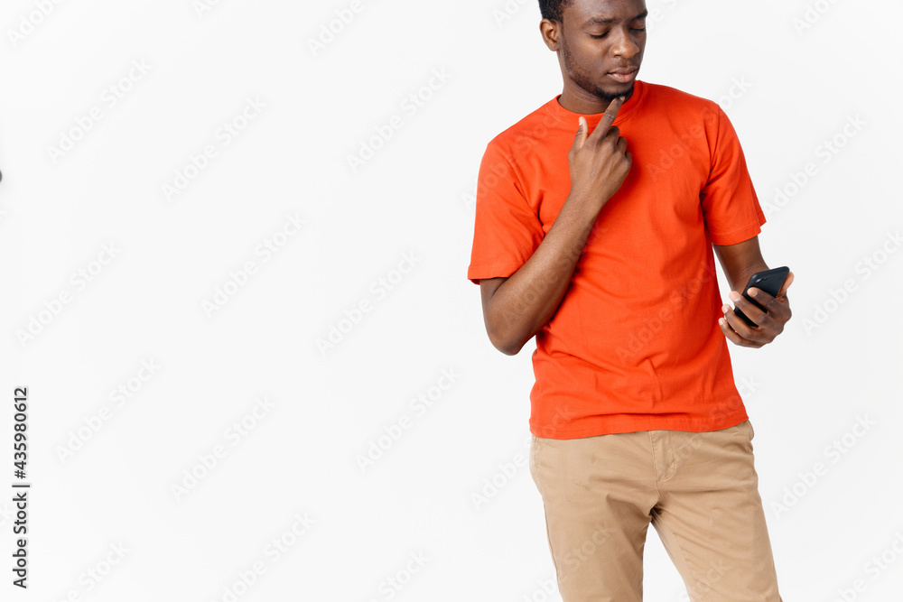 a guy in an orange T-shirt with a mobile phone on a Light background a guy in an orange T-shirt with a mobile phone on a Light background