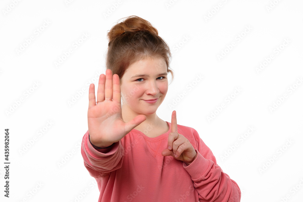 Young girl in pink casual sweatshirt shows stop sign, keeps palm forward to camera with strict expression Young girl in pink casual sweatshirt shows stop sign, keeps palm forward to camera with strict expression