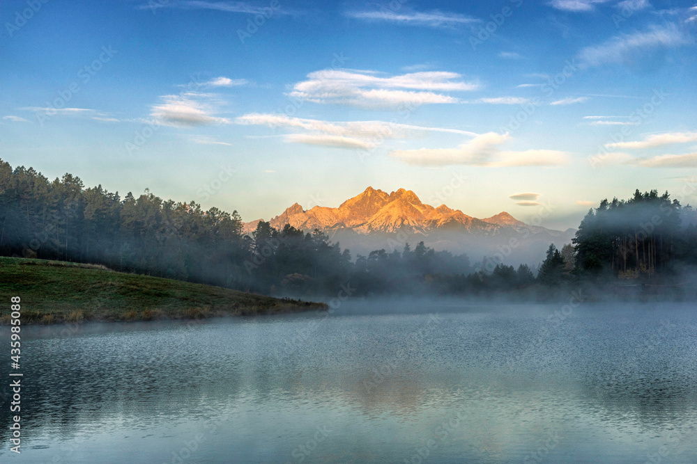 Peaceful mountain scene with calm lake, colorful trees and high peaks in a golden warm light. Scenic view of High Tatras National Park, Slovakia.