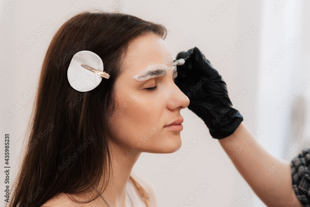 Naklejka premium The cosmetologist-brovist begins the first stage, in the correction of eyebrows, with the cleansing of the skin in the beauty salon. Professional facial care
