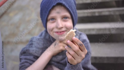 homeless boy sits on stairs in bandoned place holding bread in his hand migration homeless child with a dirty face and hands needs help Social problems custody Homeless people refugee escape from war photo