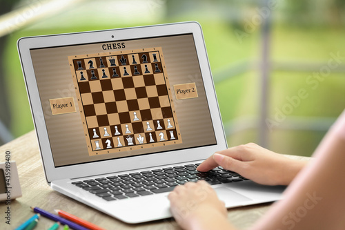 Woman playing online chess on laptop at table, closeup