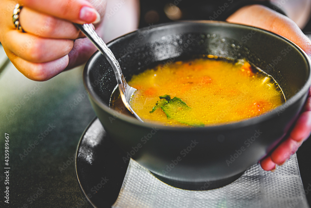 Woman hand eating chicken soup in black bowl sitting in cafe Woman hand eating chicken soup in black bowl sitting in cafe
