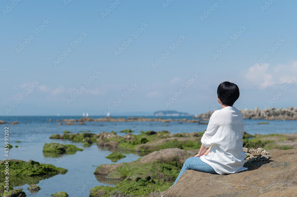 岩場に座って海を眺める女性