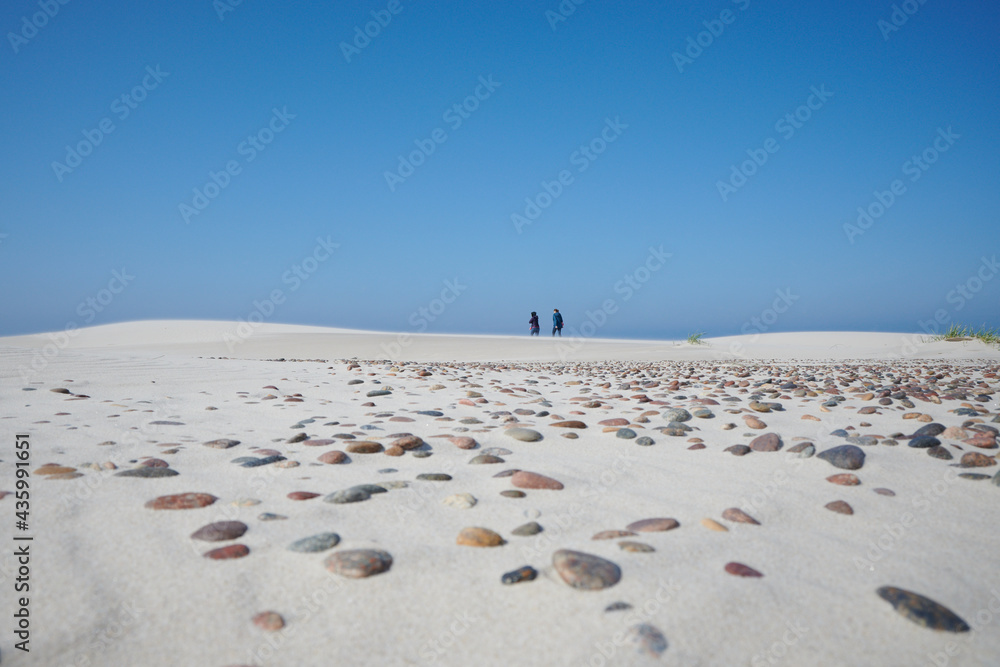 Turyści spacerują nad morzem, zdjęcie z oddali. Na pierwszym planie morski piasek w tle spacerowicze. - obrazy, fototapety, plakaty 