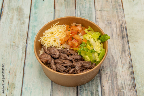 bowl of stewed beef with pieces of tomato and onion, parsley, grated cheese and lettuce