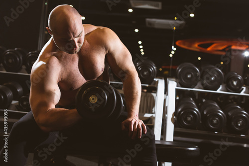 Muscular man with naked torso working out in gym doing exercises with dumbbell at biceps, strong male. Sunlight. Fitness crossfit bodybuilding concept