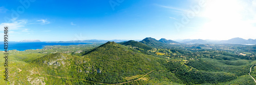 View from above, stunning aerial view of a mountain range covered by a green vegetation with a beautiful coastline bathed by the mediterranean sea. Sardinia, Italy.