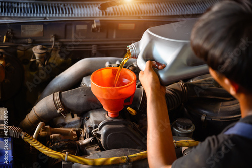 Asian auto mechanic works in auto repair shops. Pour the engine oil to change the engine oil in the garage for customers who do car repair and oil change.
