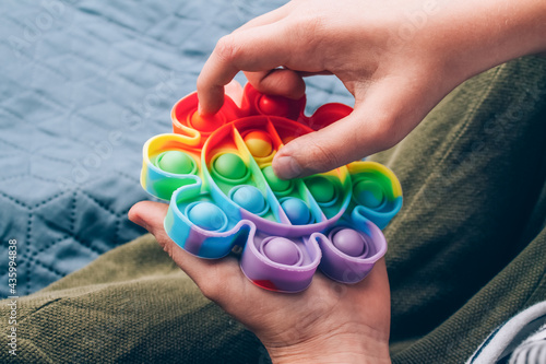Boy's hands playing with rainbow pop it fidget toy. Push bubble fidget sensory toy - washable and reusable silicone stress relief toy. Antistress toy for child with special needs