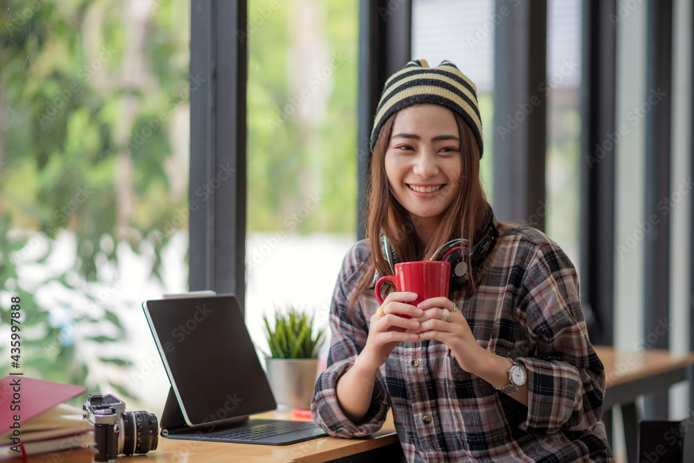 Asian woman sitting and drinking coffee at a café with a tablet. Looking at the camera.