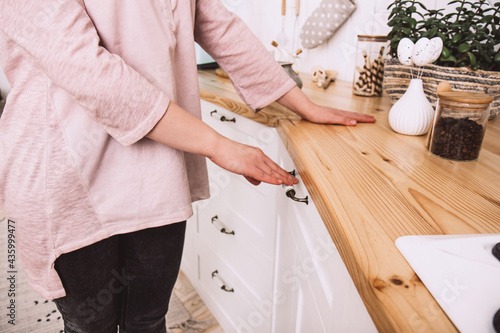 Young happy woman opens drawers on the white, light kitchen in the morning. Close up