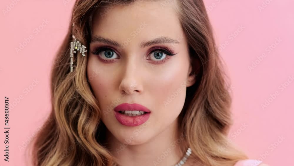 A close-up view of a beautiful young woman wearing gorgeous jewelries and hairpins is showing secret gesture to the camera standing isolated over a pink wall in the studio A close-up view of a beautiful young woman wearing gorgeous jewelries and hairpins is showing secret gesture to the camera standing isolated over a pink wall in the studio