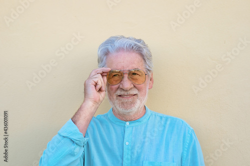 Senior white-haired and bearded man on yellow background touching sunglasses