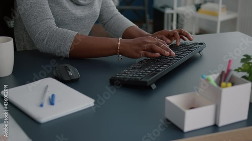 Close-up of student with black skin hands typing on keyboard searching information on internet working at business article sitting at desk table. Young woman browsing news message on computer photo