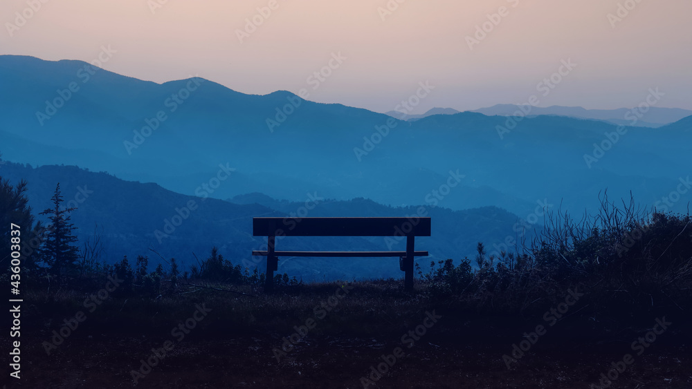 Empty wooden bench in mountain area during sunset or sunrise twilight hours. Nature tranquility landscape, no people