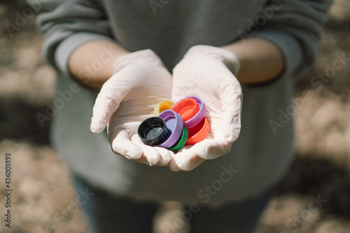 Woman hands are holding a handful of colorful plastic lids. Concept of environmental pollution  eco friendly behavior.