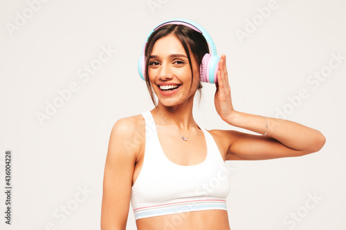 Beautiful smiling woman dressed in jeans clothes. Sexy carefree model listening music in wireless headphones. Adorable and positive female posing on grey background in studio © halayalex