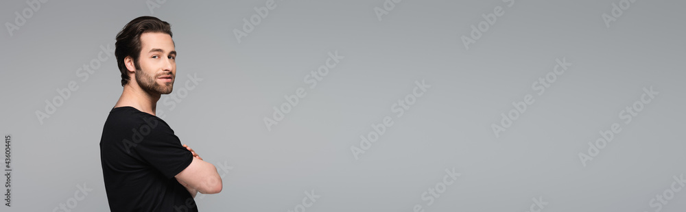 bearded and good-looking man in black t-shirt standing with crossed arms isolated on gray, banner. bearded and good-looking man in black t-shirt standing with crossed arms isolated on gray, banner.