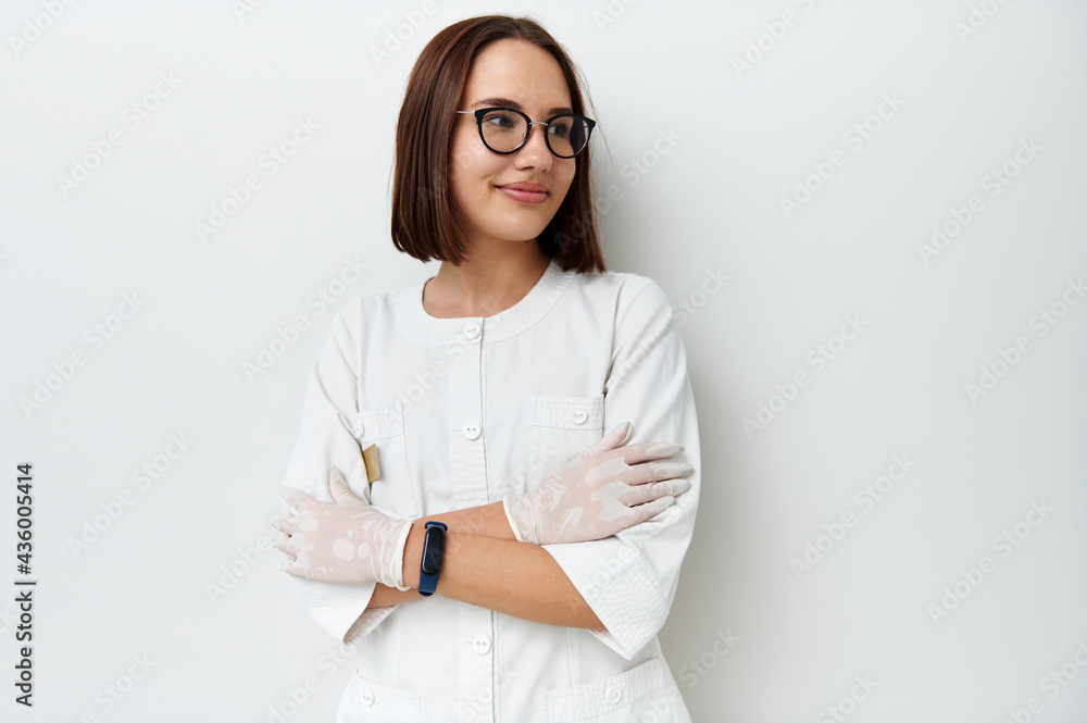 Happy young doctor intern looking away while posing against white background with crossed arms Happy young doctor intern looking away while posing against white background with crossed arms