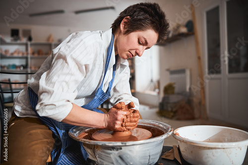Concentrated woman sculpting clay pot on pottery wheel